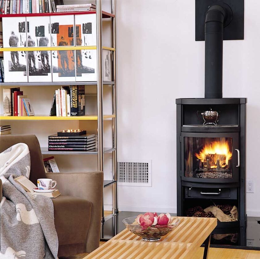 In the high-ceilinged living room, Jana and Claudio create intimacy by clustering the living room furniture around a super-efficient Rais woodburning stove and floor-to-ceiling bookshelves,